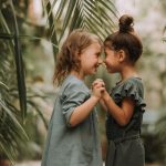 two-cute-smiling-little-girls-linen-clothes-holding-hands-walking-botanical-garden-min